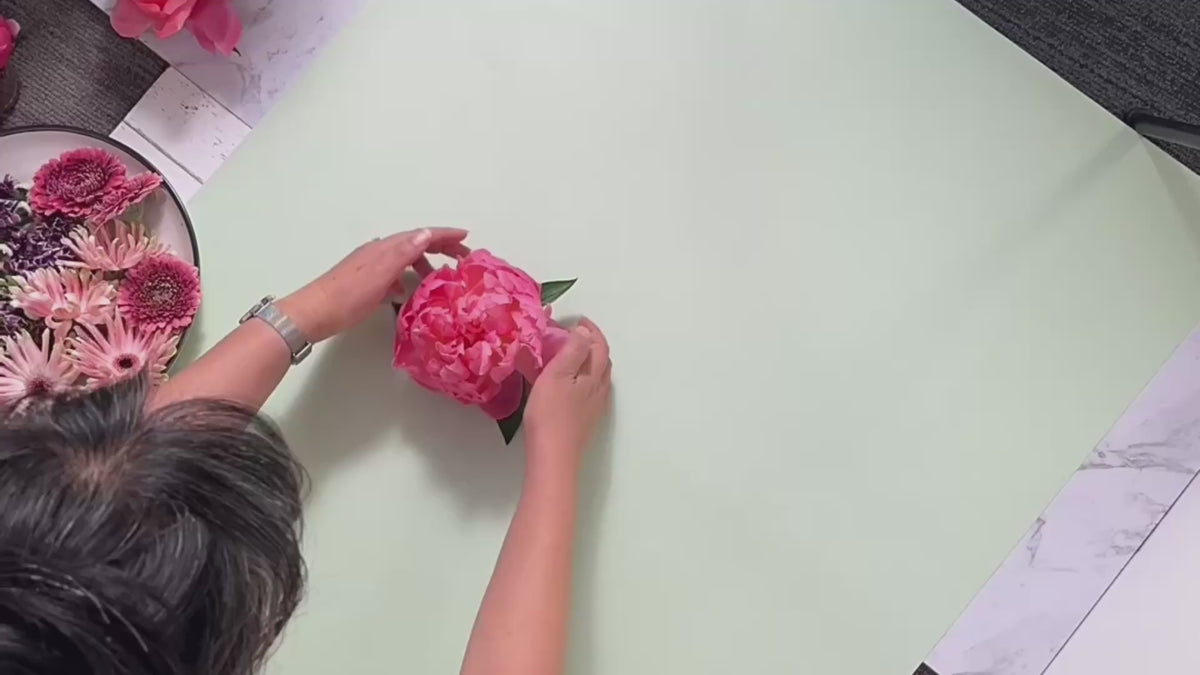 process of hand arranging a floral flatlay for a fine art photo shoot featuring pink peonies, lilacs, and gerberas