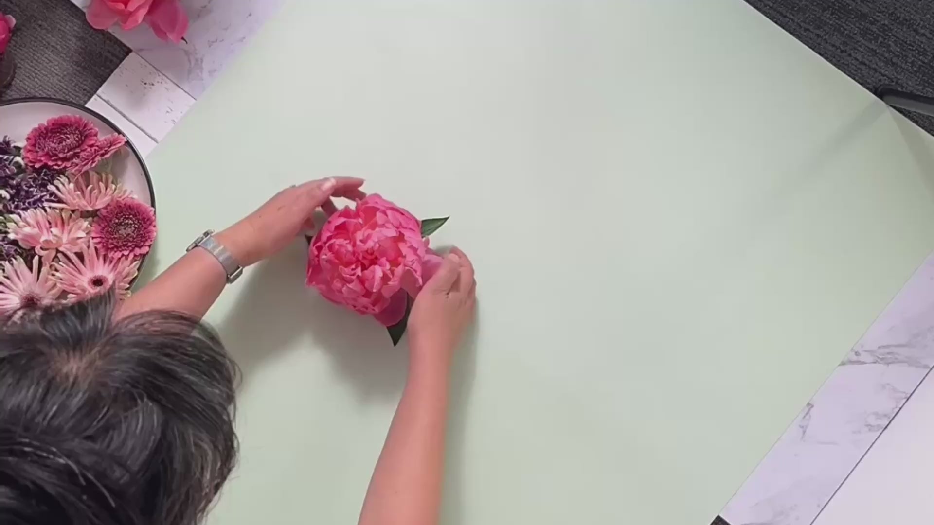 process of hand arranging a floral flatlay for a fine art photo shoot featuring pink peonies, lilacs, and gerberas